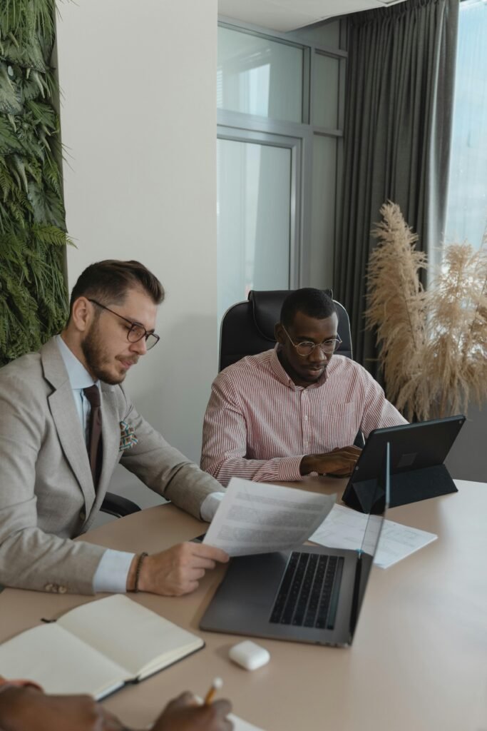 Two businessmen working collaboratively in a modern office with laptops and paperwork.